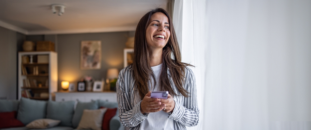 Ragazza con il telefono in mano che guarda fuori dalla finestra. | Crédit Agricole Ragazza con il telefono in mano che guarda fuori dalla finestra. | Crédit Agricole