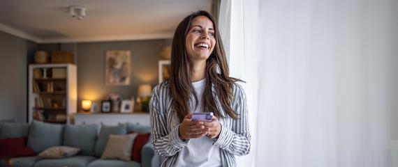 Ragazza con il telefono in mano che guarda fuori dalla finestra. | Crédit Agricole Ragazza con il telefono in mano che guarda fuori dalla finestra. | Crédit Agricole
